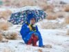 Tampak seorang anak kecil berbaju biru, dengan memakai payung serta baju tebal duduk bermain dengan salju di pegunungan Al-lawz, Tabuk, Arab Saudi.